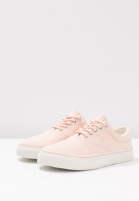 Světle růžové plátěné tenisky s bílou gumovou podrážkou, kulatou špičkou a šesti páry ok pro tkaničky. Hladký povrch, jednoduchý design.