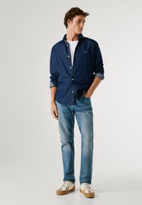 Tume sinine teksajakk, millele on sobitatud helesinised teksad ja beežid tossud. Omab üleskeeratud varrukaid ja valget ümarat kaelusega särki all.