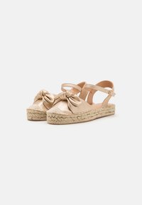 Beige espadrille sandals with a knotted satin upper, woven jute sole, and adjustable ankle strap. Smooth texture with rounded toe design.
