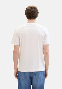 Camiseta de manga corta en gris claro con sutiles rayas horizontales, cuello acanalado y un corte relajado, combinada con jeans de mezclilla azul.