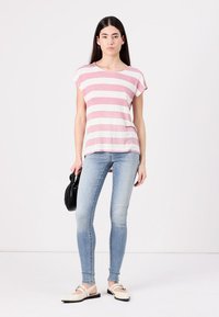 Stripet t-skjorte i lys rosa og hvit, kortermet, avslappet passform. Kombinert med lyseblå smale jeans og off-white flate sko. Svart håndveske.