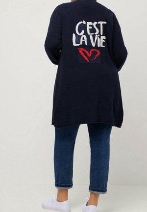 Navy niebieski sweter z dzianiny z białym napisem "C'est la vie" i czerwonym sercem na plecach, akcentowany ściągaczami i luźnym krojem.