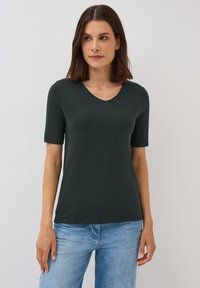 T-shirt à manches courtes vert foncé avec un design en V. Texture lisse semblable au coton, coupe près du corps, associée à un jean en denim bleu clair.