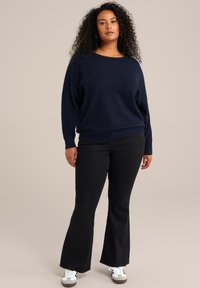 Pulover bleumarin cu decolteu larg și croi lejer, asortat cu blugi negri evazați și adidași albi cu accente negre.