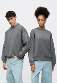 Gray oversized sweatshirts with ribbed cuffs and hems, paired with light blue relaxed-fit jeans. Matte texture and minimalist design.