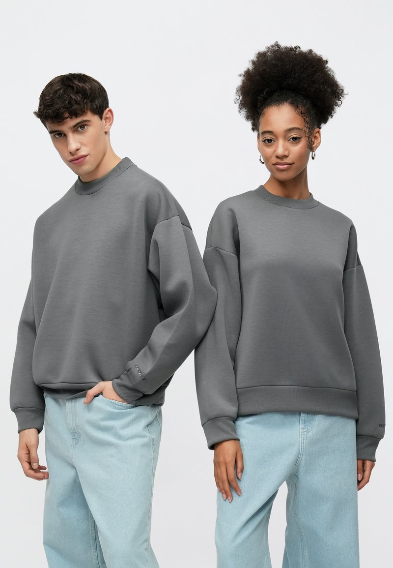 Gray oversized sweatshirts with ribbed cuffs and hems, paired with light blue relaxed-fit jeans. Matte texture and minimalist design.