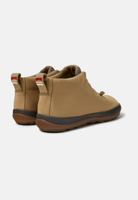 Zapatos de media caña en tono marrón, con un exterior de cuero suave, suela de goma negra y dos tiradores en el talón de tela con acentos en rojo y beige.