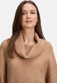 Beżowy sweter z dzianiny z szerokim golfem, prążkowaną fakturą i luźnym krojem. Posiada długie rękawy i swobodną sylwetkę.