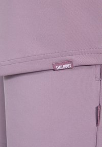 Pantaloni sportivi viola chiaro realizzati in tessuto liscio ed elastico con una piccola etichetta del marchio cucita di lato. Presentano cuciture pulite e un design minimalista.