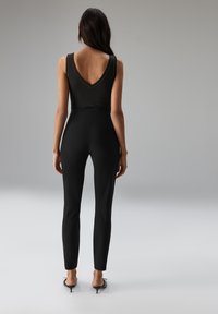 Zwarte jumpsuit met een geribbelde top met V-hals en nauwsluitende, taps toelopende pijpen. Heeft een gladde textuur en minimale hardware-accenten.