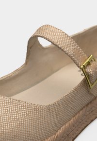 Εσπαντρίγια από μπεζ υφασμάτινο ύφασμα με λουράκι στον αστράγαλο και χρυσή αγκράφα, με εμφανές πλεγμένο χείλος σόλας από τζούτ.