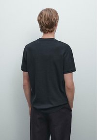 Sort ribbet t-shirt med korte ærmer, rund halsudskæring og afslappet pasform, parret med mørke bukser. Simpel tekstur, ingen synlige logoer eller mønstre.