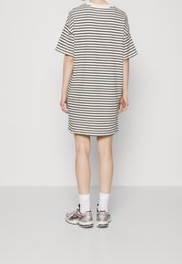 Gestreiftes Baumwoll-T-Shirt-Kleid in Creme und Schwarz, lockere Passform mit kurzen Ärmeln, knielang, kombiniert mit silbernen Sneakern und weißen Socken.