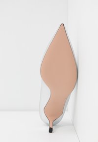 Escarpin blanc en cuir avec un bout pointu et une surface lisse. La semelle est marron clair avec un accent noir au niveau du talon.