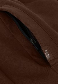 Bruine stof met een fijne textuur met een zakje met rits. Een label met de tekst "spiritbulb studios" zit aan de rand nabij de rits.