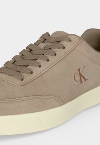 Μπεζ σουεδ sneaker με μπεζ κορδόνια, κρεμ σόλα και καφέ λογότυπο "cK" στη πλευρά.