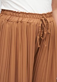 Pleated brown skirt with an elastic waistband and drawstring. Made of lightweight fabric, features vertical folds for texture and flow.