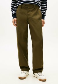 Olijfgroene recht-zittende broek van katoen, met een knoopsluiting en zijzakken, gecombineerd met witte sneakers en een gestreepte trui.