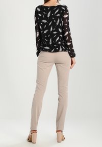 Black sheer blouse with white feather pattern, paired with beige slim-fit trousers and nude high-heeled sandals, model viewed from back.