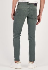 Kapea hirvensarven farkut hillityn vihreässä denimmissä. Ominaisuuksiin kuuluu viisi taskua, huomaamaton ompelu ja keski-nostoinen vyötärö, yhdistettynä valkoisiin tennareihin.