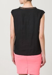 Schwarzes ärmelloses Oberteil mit einem runden Ausschnitt und subtiler Textur, kombiniert mit einem rosa Jeansrock mit Gesäßtaschen und einem Schlitz.