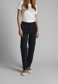 T-shirt blanc à manches courtes avec broderie florale, associé à un pantalon droit bleu marine et des baskets beiges avec des accents marron foncé.