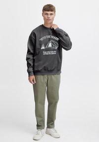Sudadera gris con gráfico blanco de camping, de corte holgado, con puños de canalé. Combinada con pantalones verde oliva y zapatillas blancas. Diseño simple, textura suave.