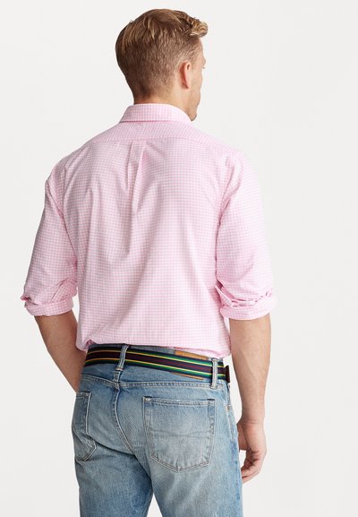 Camisa de cuadros rosa claro con mangas enrolladas, combinada con jeans azules y un cinturón de rayas multicolores, que muestra un estilo casual.