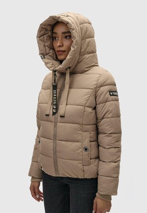 Frau trägt eine beige gesteppte Kapuzenjacke mit Reißverschluss und Taschen, steht vor einem einfarbigen hellen Hintergrund und blickt nach links.