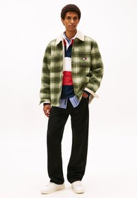 Πράσινο καρό σακάκι με κολάρο σε εκρού χρώμα πάνω από πολύχρωμη ριγέ πόλο, συνδυασμένο με μαύρο παντελόνι με λεπτό μοτίβο και λευκά αθλητικά παπούτσια.