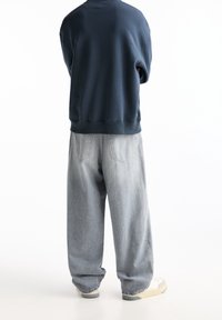 Felpa blu navy con colletto rotondo, abbinata a jeans in denim grigio chiaro a vestibilità morbida e scarpe da ginnastica bianche, vista da dietro.