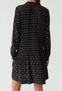 Abito nero con maniche lunghe, caratterizzato da un motivo geometrico in rosso e beige, tessuto testurizzato e orlo svasato.