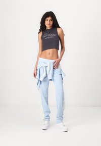 Top scurt de culoare gri închis cu un grafic alb, asociat cu pantaloni de trening de culoare albastră deschisă, având dungi laterale în culori pastelate și adidași albi.