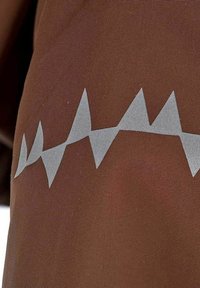 Brun tyg med ett zigzag-mönster i silver, som visar en slät textur och ett mönstrat accent längs ytan.