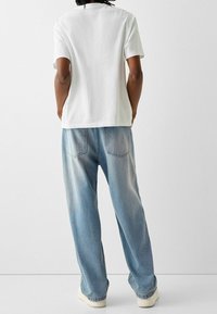 Bílé bavlněné tričko s krátkými rukávy, doplněné volnějšími světle modrými džínami s vybledlou texturou a zadními kapsami.