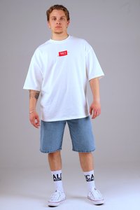 White oversized T-shirt with red logo, blue denim shorts, white sneakers, and white socks with black lettering. Simple design and relaxed fit.