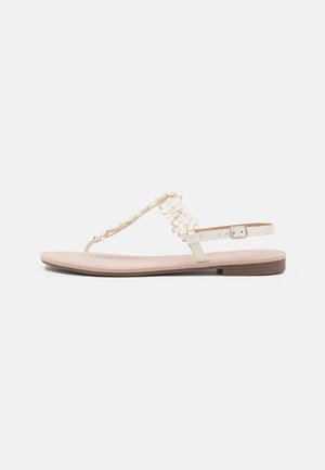 Flat sandal in pale cream with floral accents on the strap, featuring a toe post design and a light tan textured footbed. Adjustable ankle strap.