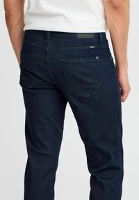 Mörkblå denimjeans med en figurnära design, som har två bakfickor, en läderpatch på midjebandet och subtila sömnadsdetaljer.