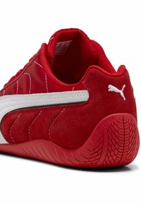 Roter Sportschuh mit Obermaterial aus Wildleder und Synthetik. Verfügt über einen weißen Streifen, eine strukturierte Gummisohle und ein gepolstertes Innenmaterial für Komfort.