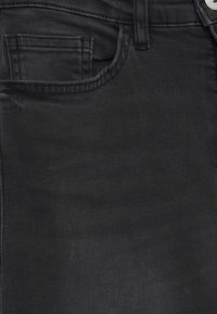 Gros plan sur un tissu en denim noir montrant la poche avant, la petite poche à monnaie, la passant de ceinture et le bouton métallique à la taille du jean.