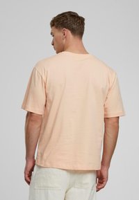 Pfirsichfarbene Baumwoll-T-Shirt mit kurzen Ärmeln, Rundhalsausschnitt und lockerer Passform, ausgestattet mit einer glatten Textur und ohne sichtbare Muster oder Logos.