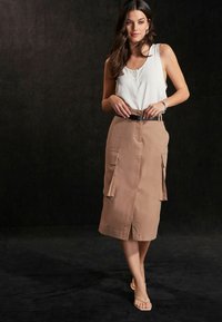 Knælængde beige cargo-nederdel med to frontlommer, en slids foran og et sort bælte. Sammen med en hvid ærmeløs top.