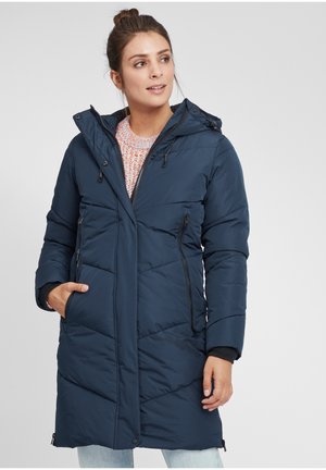 Navy puffer coat with a hood, featuring quilted design, zippered front pockets, and ribbed cuffs, worn over a colorful knitted sweater.