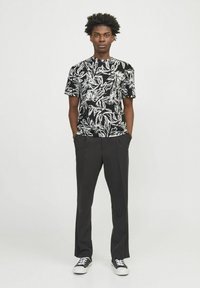 Sort T-shirt med korte ærmer og hvidt blomsterprint, kombineret med løse sorte bukser og sort-hvide sneakers. Enkel design og teksturer.
