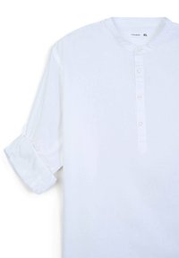 Camicia bianca a maniche lunghe con colletto alla cinese, pattina con bottoni e maniche arrotolate. Realizzata in tessuto leggero con una texture liscia.