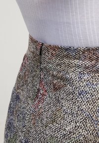Pantalon en tissu texturé multicolore avec une taille ajustée et un léger éclat, présentant un motif prononcé aux teintes pastel.