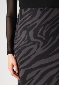 Jupe à rayures zèbre noires et grises avec une texture lisse, accompagnée d'un haut noir à manches longues transparent, agrémenté d'un petit nœud.