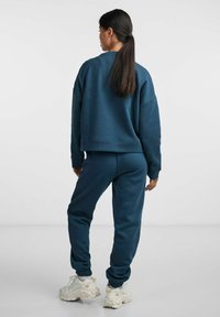 Navy blue sweatshirt with a relaxed fit and ribbed cuffs paired with matching joggers; both made of soft material. Chunky white sneakers.