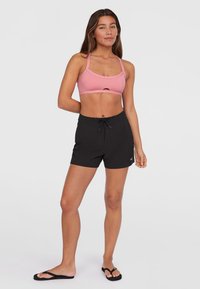 Rosa idretts-bh med utskjæringsdetalj, sammen med svarte shorts med snor i livet og svarte flip-flops. Glatt stoff, uformell passform.