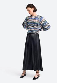 Strickpullover mit einem mehrfarbigen, abstrakten Muster; plissierter schwarzer Midirock; schwarze High Heels mit Knöchelriemen.